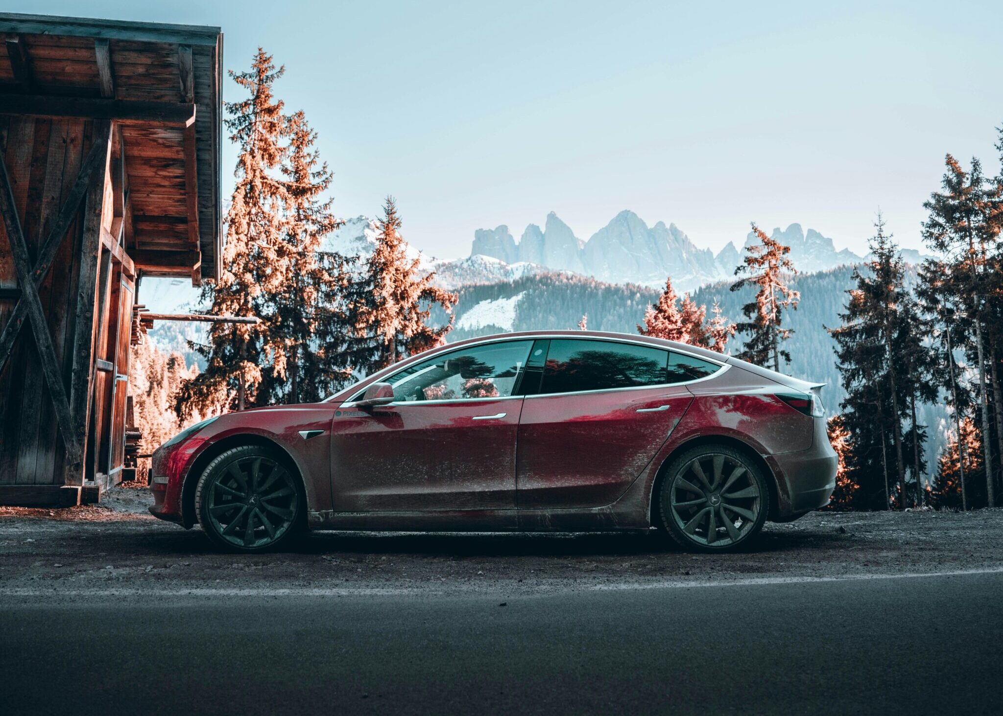 Stunning view of a red electric car parked by a mountain cabin in snowy winter landscape.