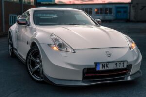 A white Nissan 370Z sports car parked in an urban setting in Norrtälje, Sweden. Genuine vs. Aftermarket